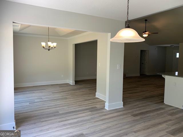 unfurnished dining area with baseboards, ceiling fan with notable chandelier, wood finished floors, and ornamental molding