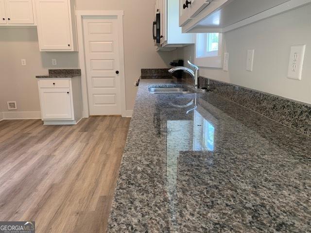 kitchen with dark stone countertops, baseboards, light wood-style flooring, a sink, and white cabinets