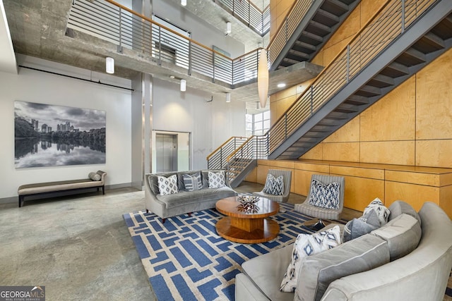 living area featuring wooden walls, baseboards, a high ceiling, stairs, and concrete flooring