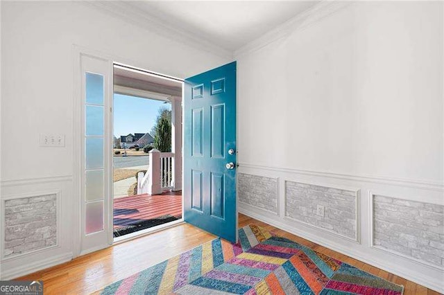 foyer with wood finished floors, ornamental molding, wainscoting, and a decorative wall