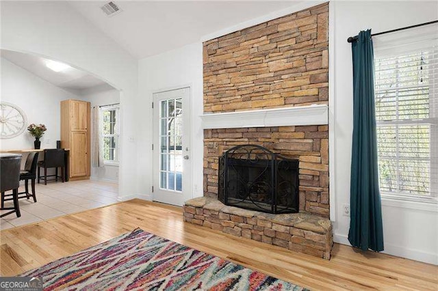 living area featuring visible vents, wood finished floors, arched walkways, a fireplace, and lofted ceiling