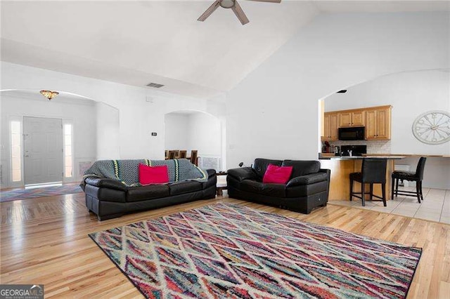 living area featuring visible vents, ceiling fan, light wood-type flooring, arched walkways, and high vaulted ceiling