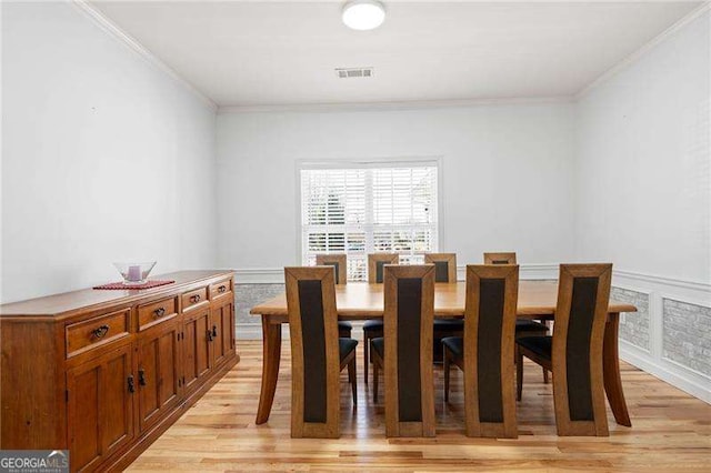 dining space featuring wainscoting, visible vents, light wood-style flooring, and ornamental molding