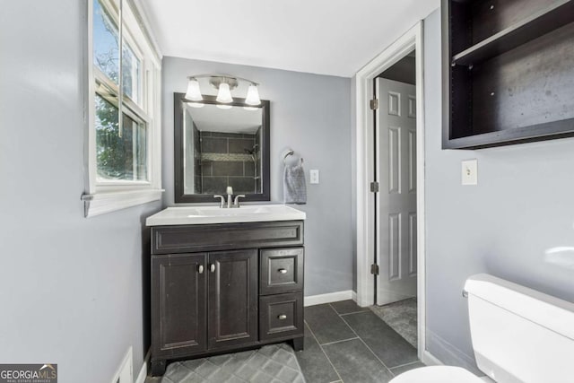 bathroom featuring tile patterned floors, toilet, tiled shower, baseboards, and vanity