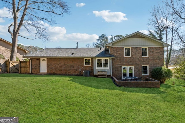 rear view of property featuring brick siding, central AC unit, a lawn, and fence