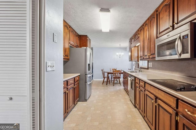 kitchen with light countertops, appliances with stainless steel finishes, a notable chandelier, a textured ceiling, and a sink