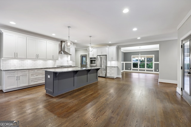 kitchen with wall chimney range hood, dark wood-style flooring, appliances with stainless steel finishes, white cabinets, and a kitchen island with sink