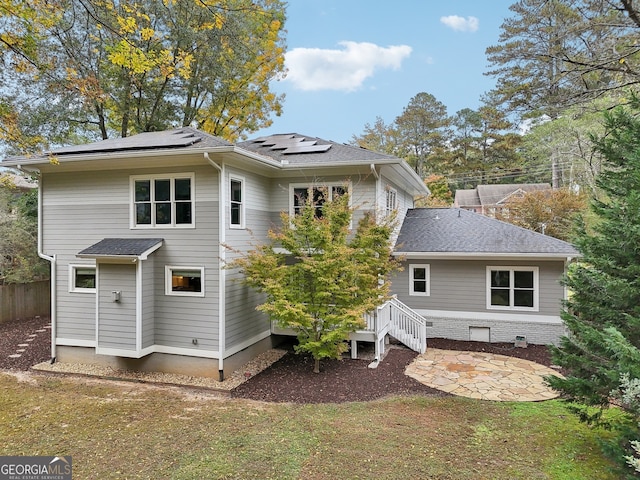 rear view of property featuring roof mounted solar panels, a lawn, a shingled roof, and a patio