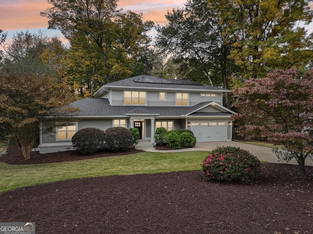 traditional-style home with a yard, roof mounted solar panels, a garage, and driveway