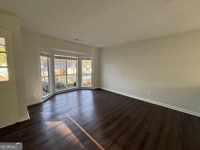 empty room with baseboards, a healthy amount of sunlight, and dark wood-style flooring