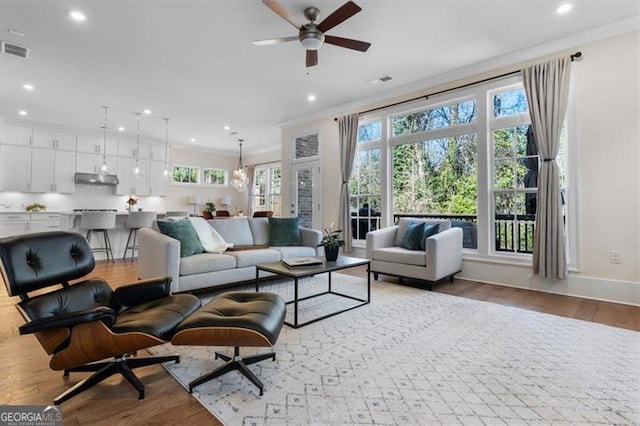 living area with wood finished floors, baseboards, visible vents, recessed lighting, and ornamental molding