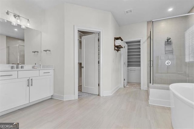 bathroom featuring vanity, baseboards, a stall shower, a freestanding bath, and a walk in closet