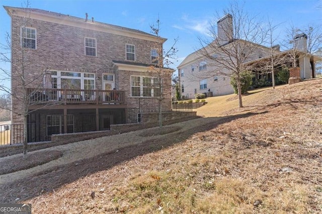 rear view of house featuring brick siding, a deck, and fence