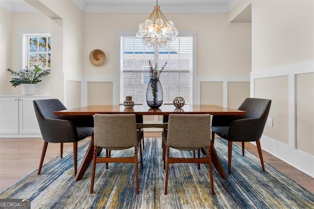 dining space featuring an inviting chandelier, a decorative wall, wood finished floors, and ornamental molding