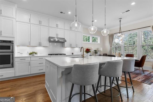 kitchen featuring ornamental molding, visible vents, under cabinet range hood, and a sink