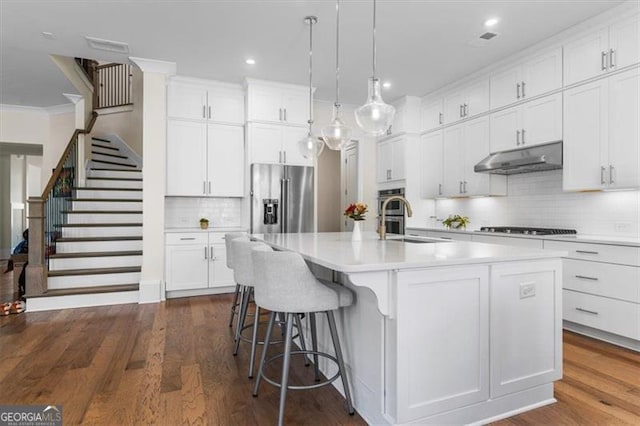 kitchen featuring an island with sink, ornamental molding, under cabinet range hood, a sink, and appliances with stainless steel finishes