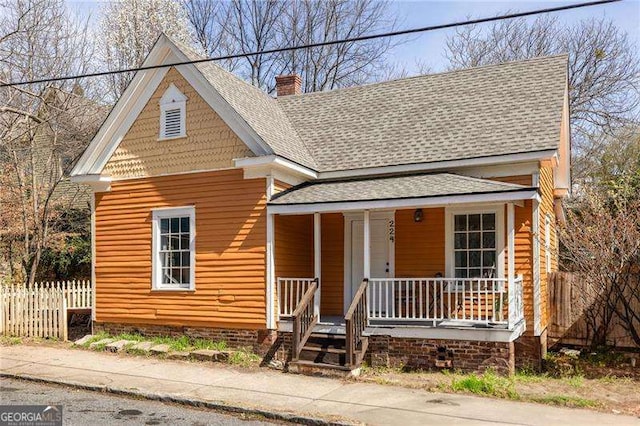 view of front of house featuring covered porch, a chimney, roof with shingles, and fence