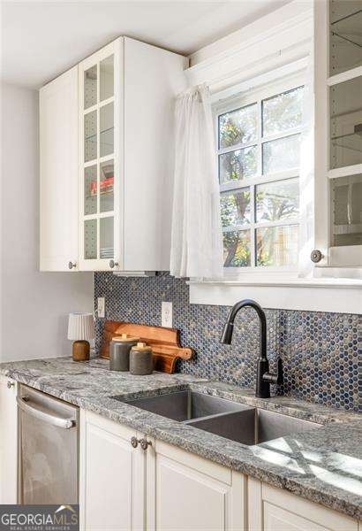 kitchen with decorative backsplash, white cabinets, stainless steel dishwasher, and a sink