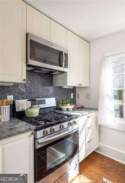 kitchen featuring wood finished floors, baseboards, white cabinets, appliances with stainless steel finishes, and tasteful backsplash