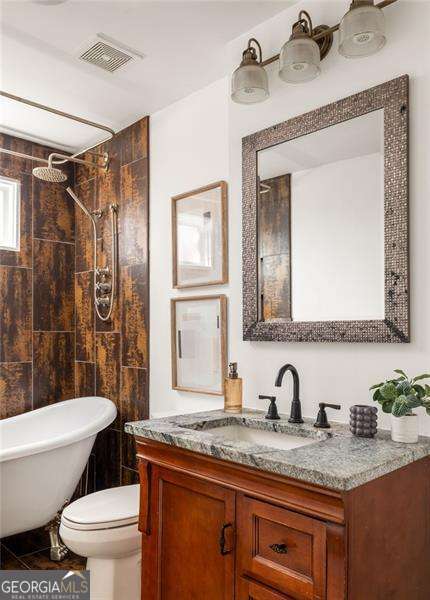 bathroom with visible vents, toilet, a tub, tiled shower, and vanity