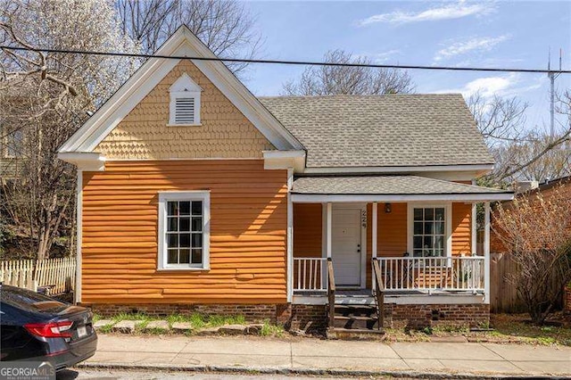 view of front facade featuring fence, covered porch, and a shingled roof