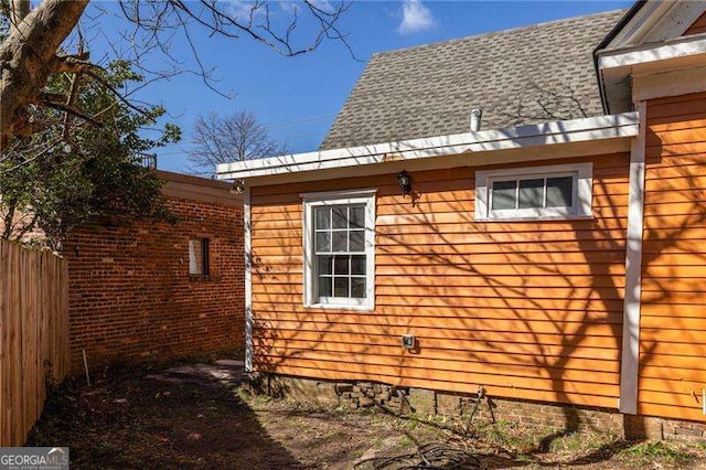 view of side of property featuring a shingled roof and fence