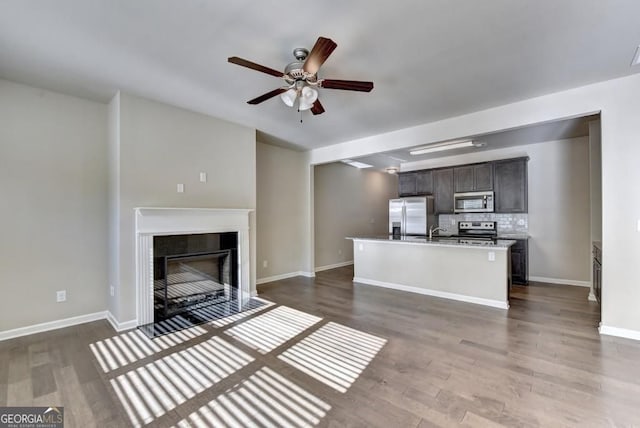 unfurnished living room featuring wood finished floors, baseboards, a fireplace with flush hearth, a sink, and ceiling fan