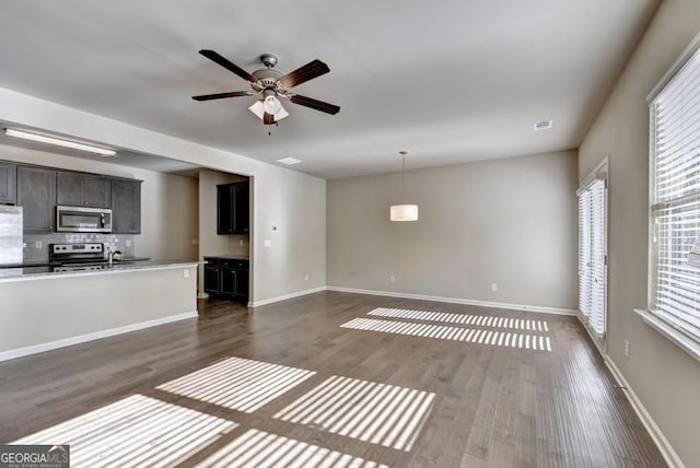 unfurnished living room featuring a wealth of natural light, baseboards, and dark wood-type flooring