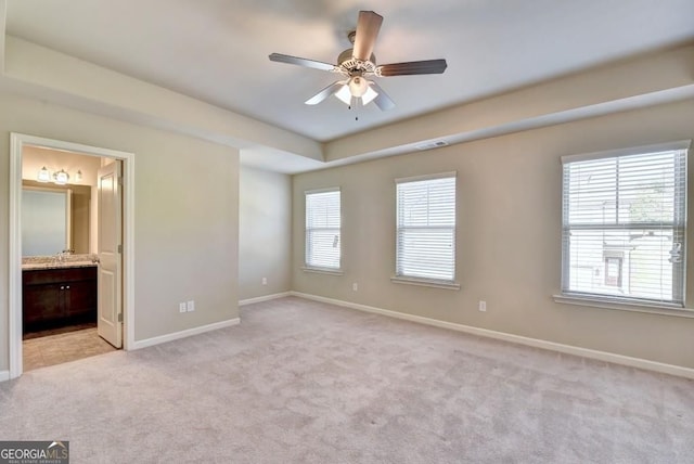 unfurnished bedroom featuring visible vents, light carpet, ensuite bath, baseboards, and a raised ceiling