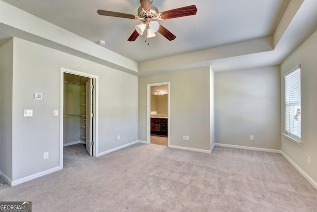 unfurnished bedroom with baseboards, a raised ceiling, light colored carpet, and a spacious closet