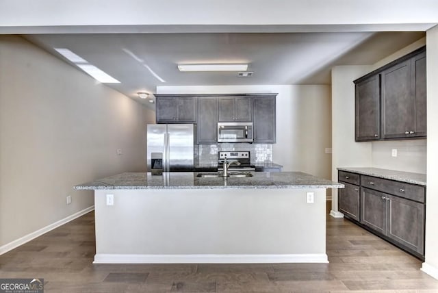 kitchen featuring light stone counters, a sink, dark brown cabinetry, appliances with stainless steel finishes, and tasteful backsplash