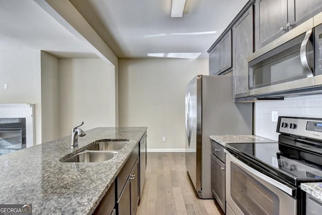 kitchen with backsplash, stone counters, appliances with stainless steel finishes, light wood-style floors, and a sink