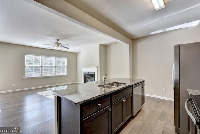 kitchen featuring a sink, a glass covered fireplace, stainless steel appliances, light wood-style floors, and dark brown cabinets