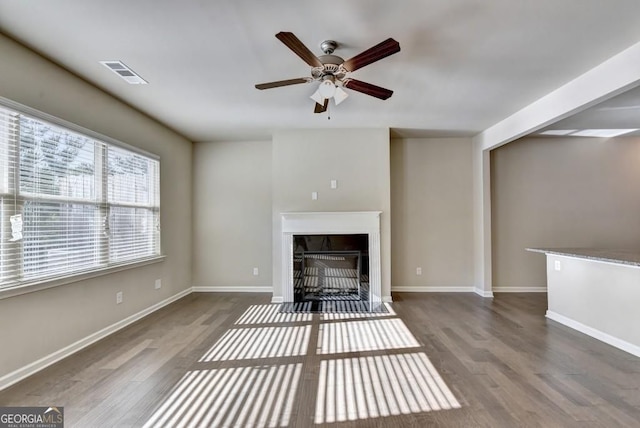 unfurnished living room featuring a fireplace with flush hearth, wood finished floors, visible vents, and baseboards