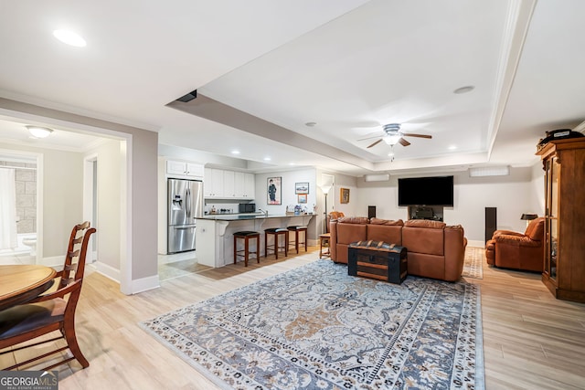 living area with light wood-type flooring, ceiling fan, a raised ceiling, and recessed lighting