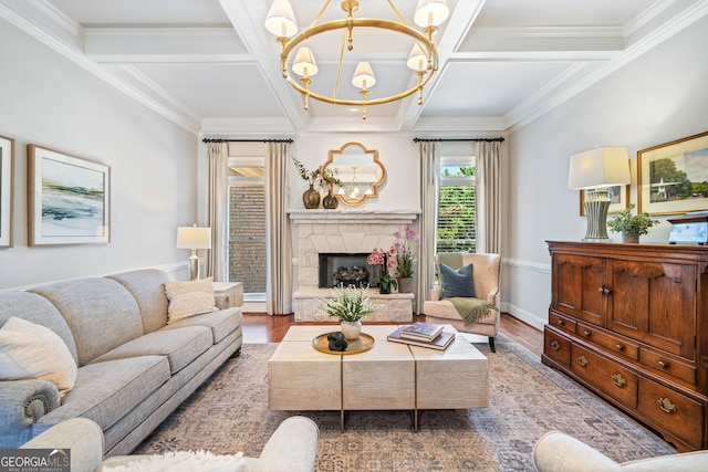 living room featuring a stone fireplace, an inviting chandelier, ornamental molding, coffered ceiling, and wood finished floors