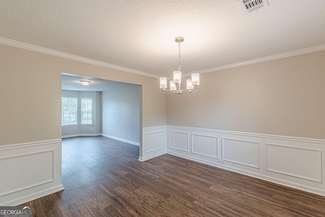 spare room featuring dark wood-type flooring, visible vents, crown molding, wainscoting, and a notable chandelier