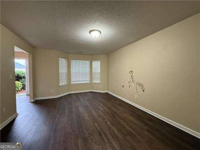 empty room featuring baseboards, a textured ceiling, and dark wood-style flooring