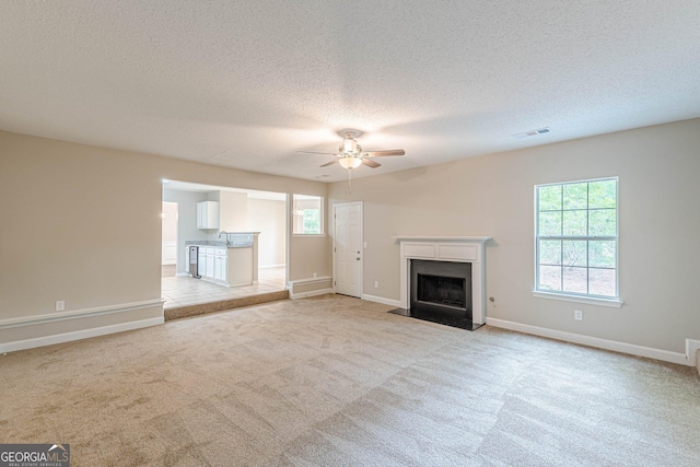 unfurnished living room featuring a ceiling fan, light carpet, a fireplace, and visible vents