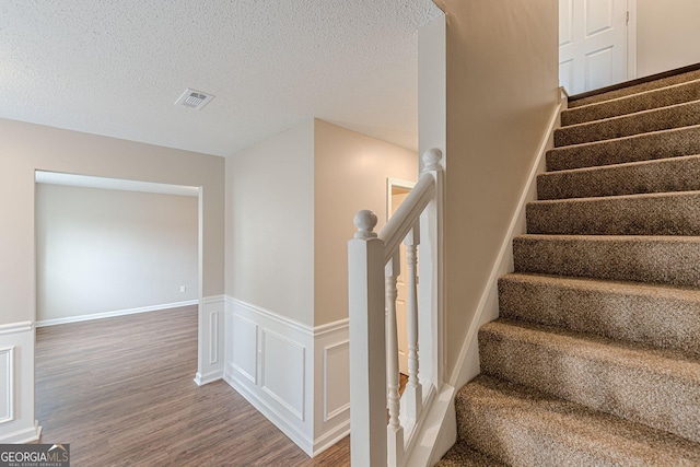 staircase with a textured ceiling, a wainscoted wall, visible vents, and wood finished floors