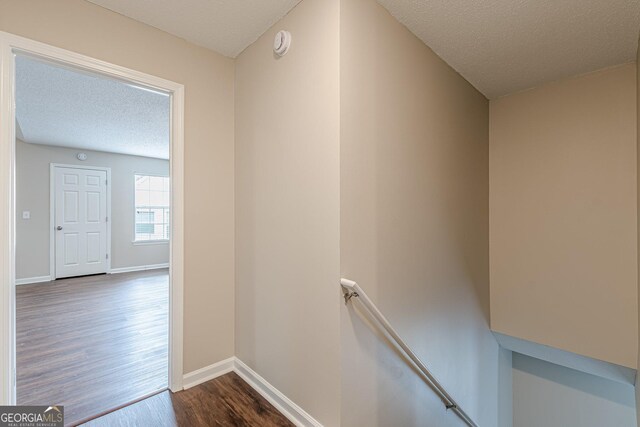 hallway with baseboards, an upstairs landing, a textured ceiling, and dark wood-type flooring