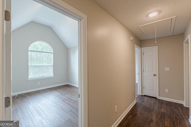 hallway with a textured ceiling, attic access, vaulted ceiling, dark wood-style floors, and baseboards