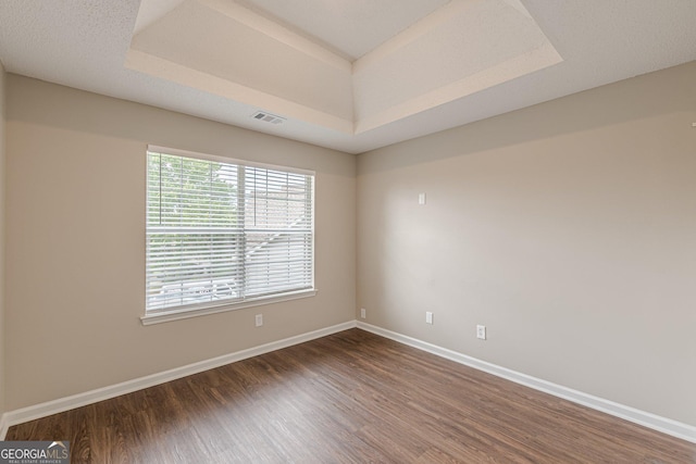 unfurnished room featuring baseboards, a tray ceiling, visible vents, and wood finished floors