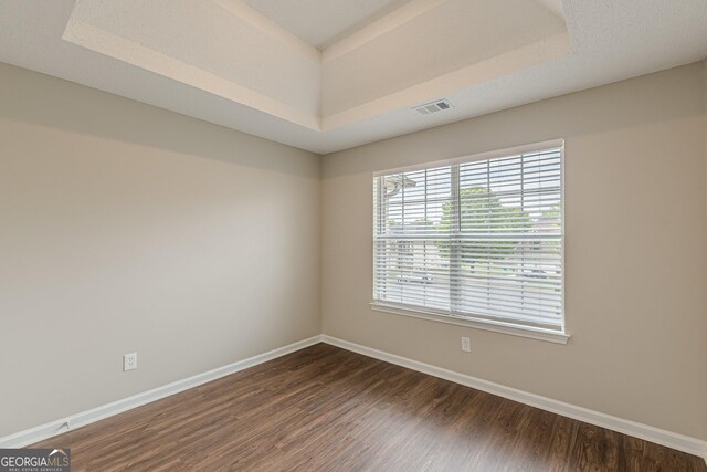 unfurnished room featuring baseboards, a raised ceiling, visible vents, and dark wood-type flooring