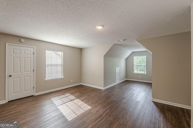 additional living space featuring baseboards, dark wood-style flooring, visible vents, and a textured ceiling