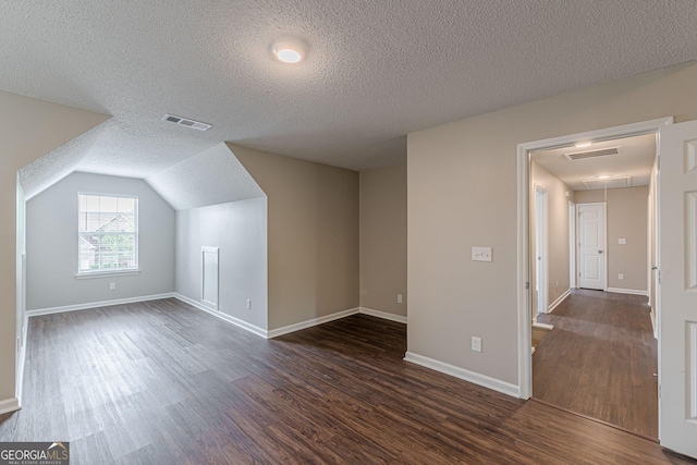 additional living space with dark wood-style flooring, visible vents, attic access, and a textured ceiling