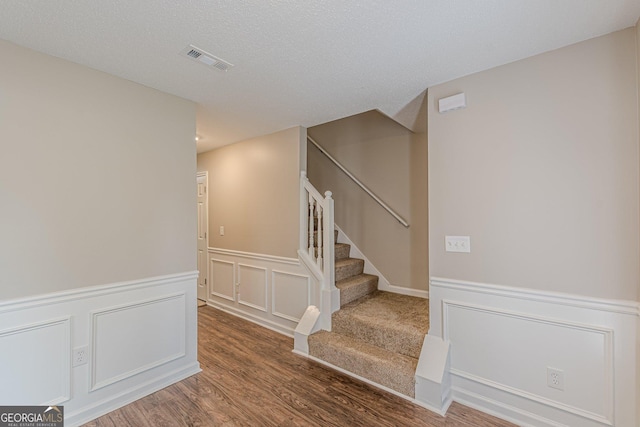 staircase featuring a decorative wall, a wainscoted wall, visible vents, and wood finished floors