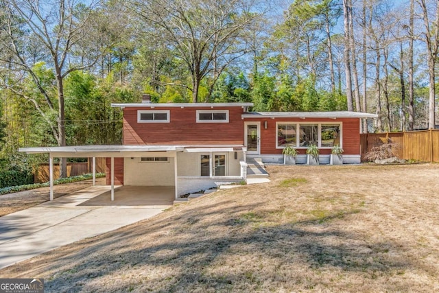 split level home featuring an attached carport, fence, concrete driveway, and a chimney
