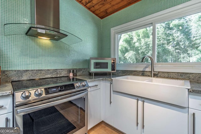 kitchen featuring appliances with stainless steel finishes, wood ceiling, a sink, white cabinetry, and wall chimney range hood