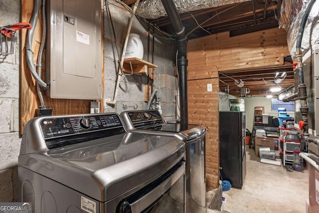 washroom with electric panel, washer and clothes dryer, and wood walls